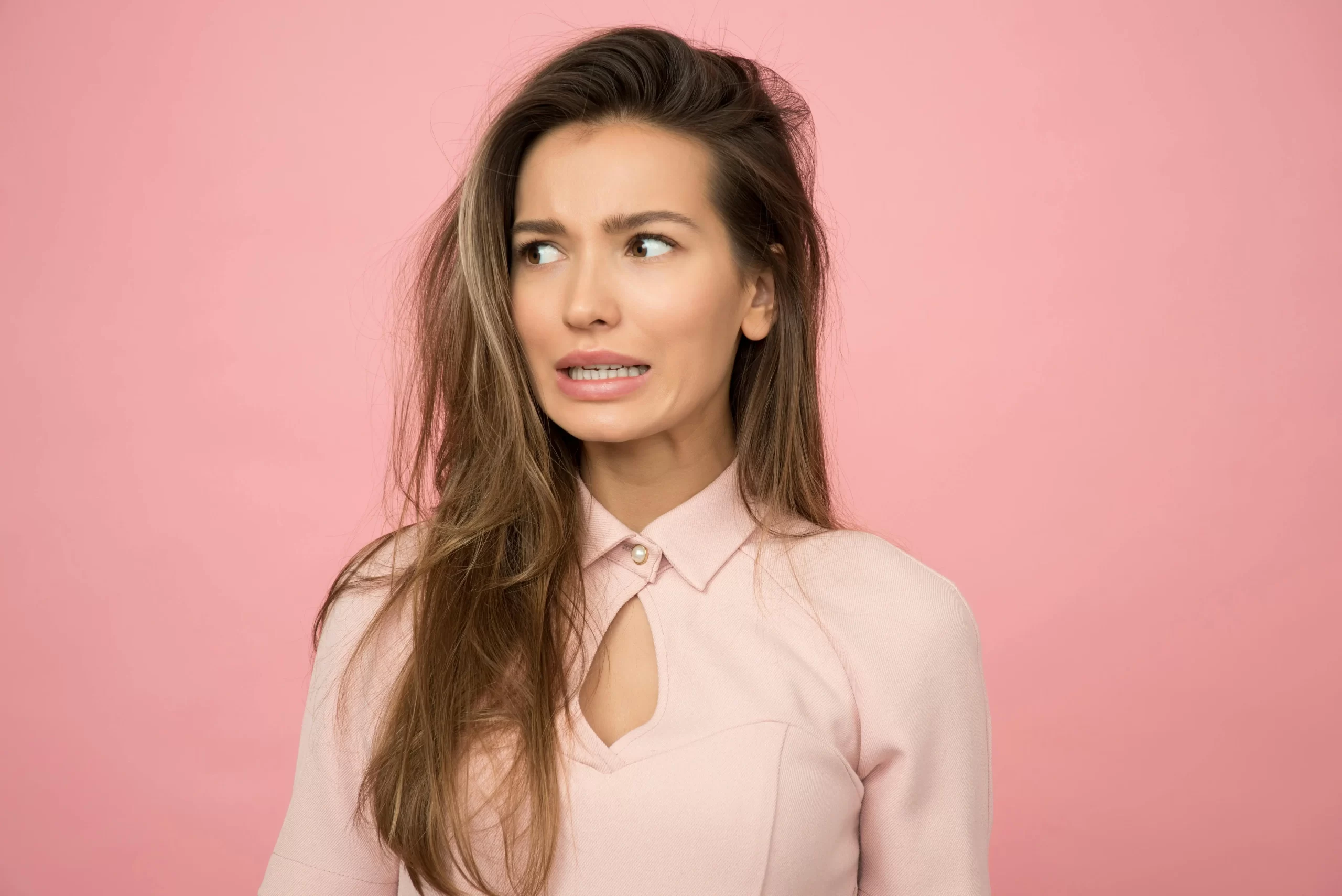 A woman making a worried face against a pink background.