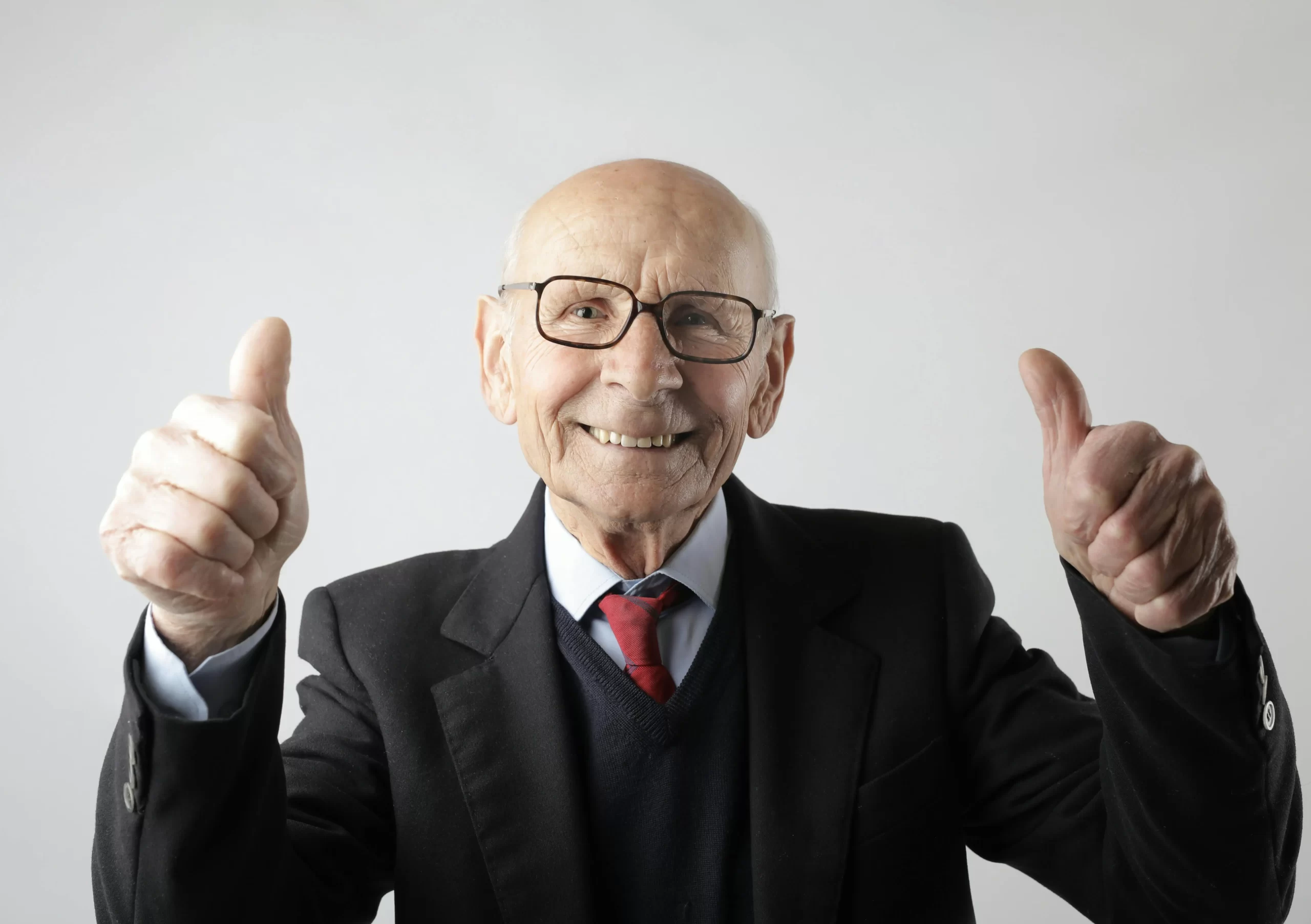 An elderly bald man giving two thumbs up.