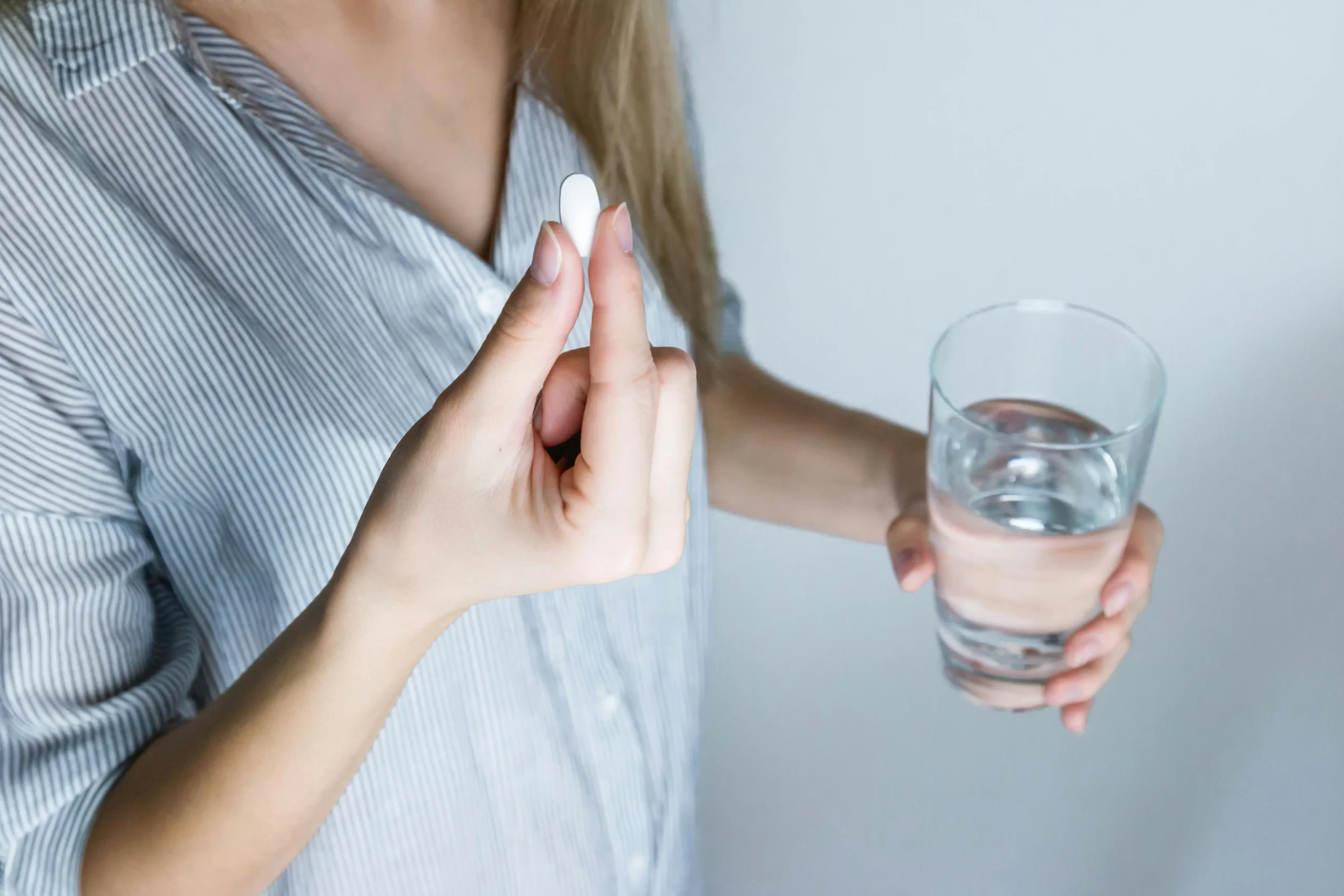 A woman with a glass of water taking a pain killer medication for her herniated disc nerve pain.